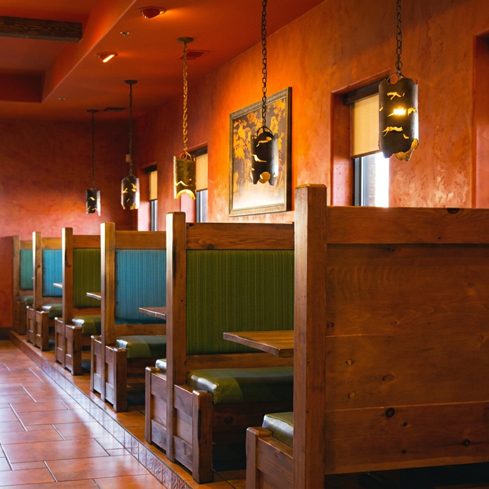 A row of wooden booths with green and blue cushions in a restaurant with orange walls and tiled floors.
